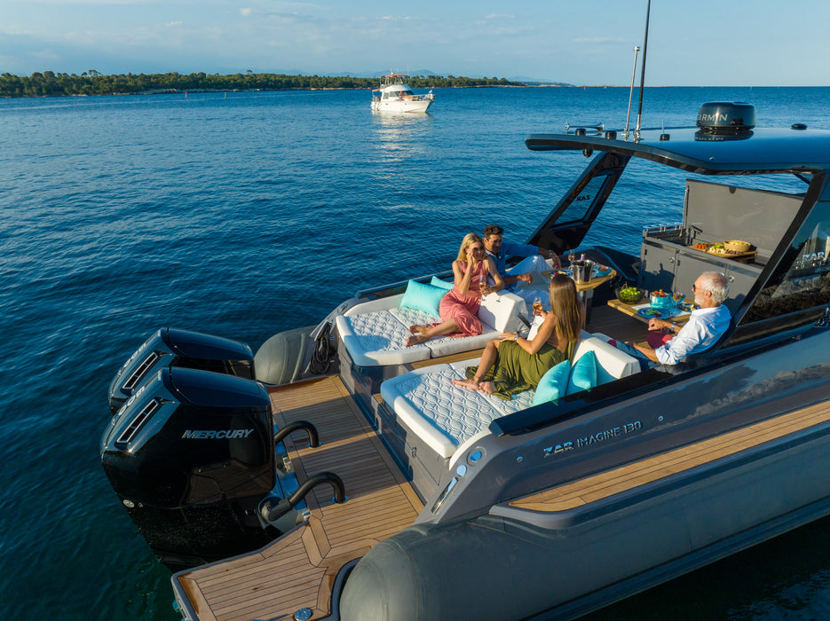 A Zodiac 1100 outboard motor boat on open water with several people relaxing on the rear deck seating. The boat has a gray hull, wood-look flooring, a black hardtop, and black Mercury outboard motors.